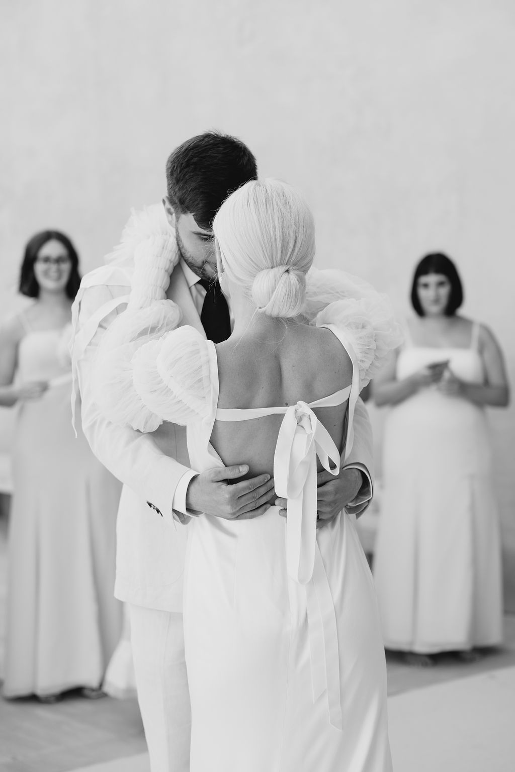 Black and white wedding ceremony photograph with bridesmaids in background.
