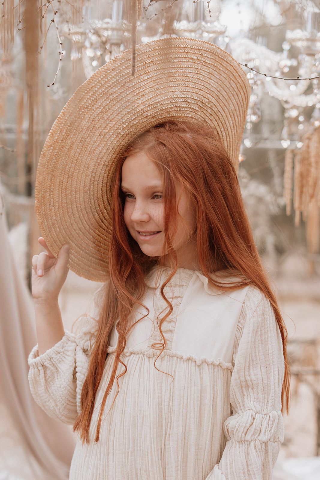 Close-up portrait with wide-brim hat and vintage dress under crystal lighting.