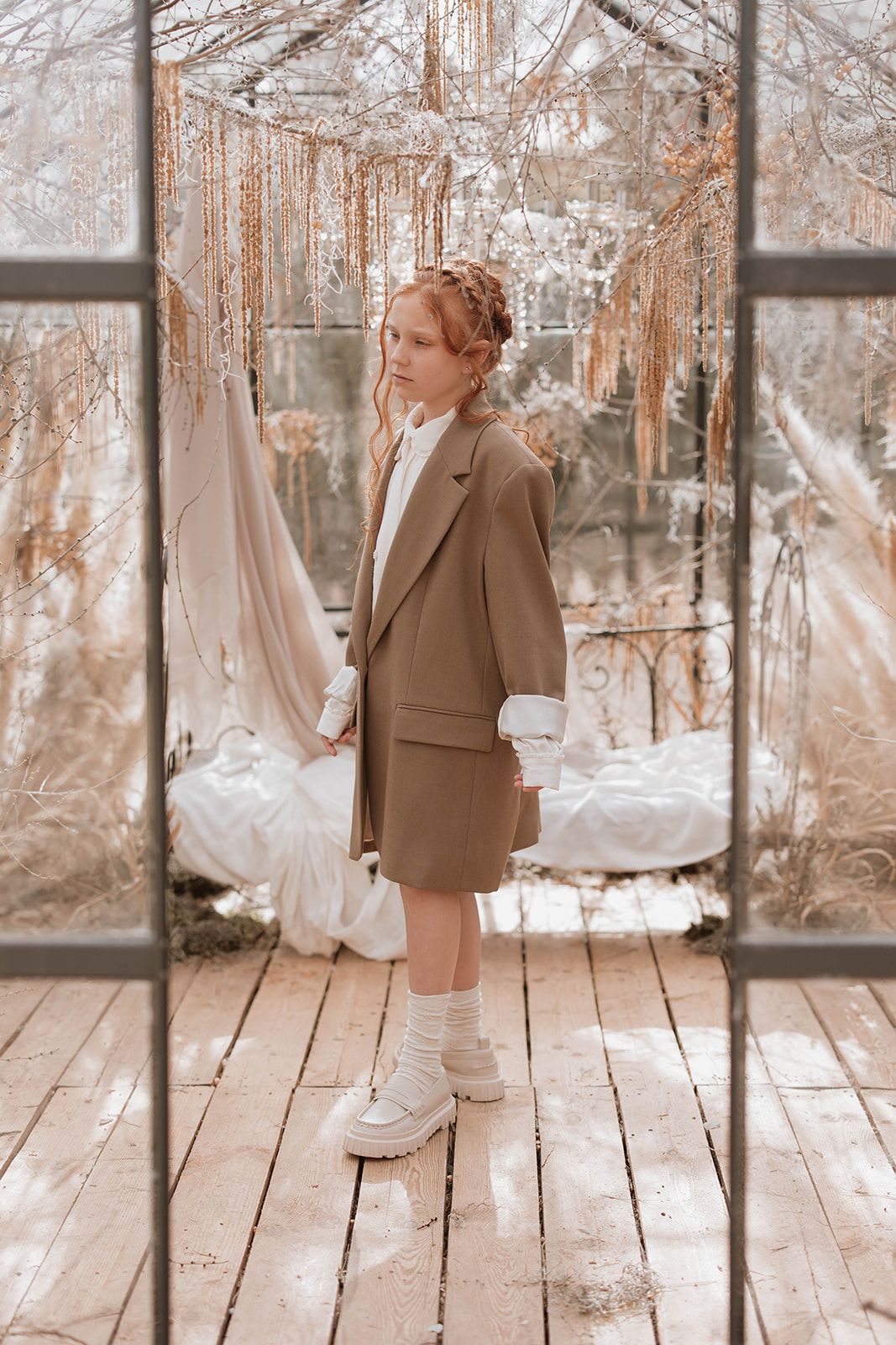 Artistic portrait in a greenhouse with ethereal winter decor and natural light filtering through glass panels.