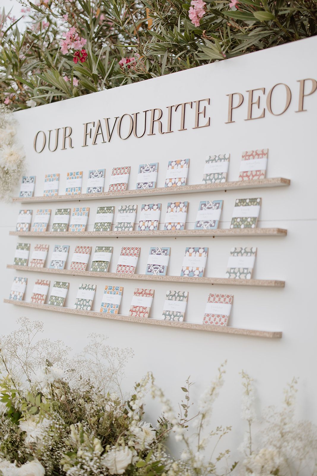 Wedding seating chart display titled 'Our Favourite People' with rows of cards against a white wall.