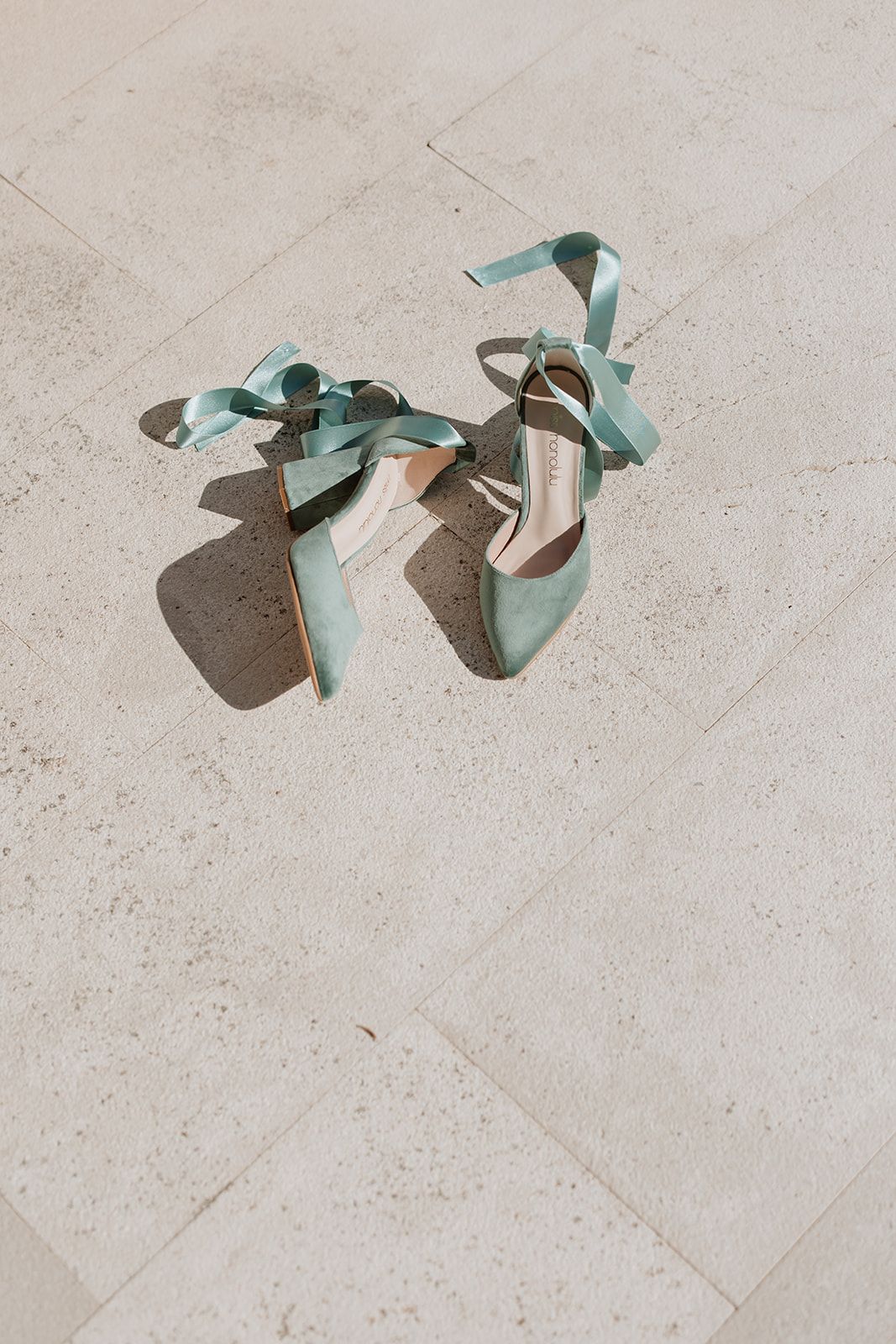 Mint green strappy shoes casting shadows on light stone flooring.