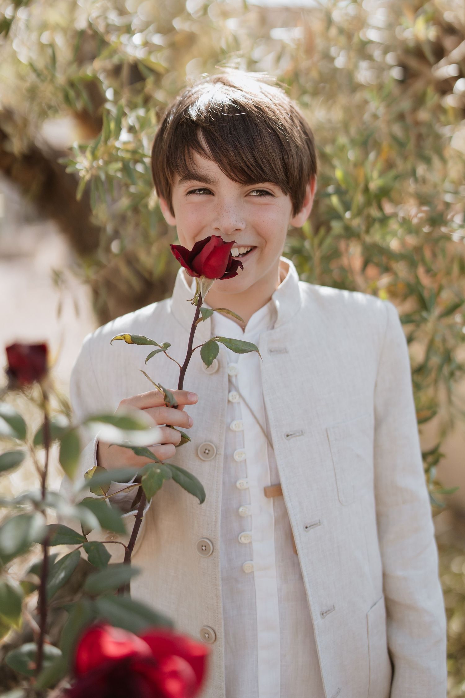 A series of photos showing someone in a white formal jacket smelling red roses in a garden setting.