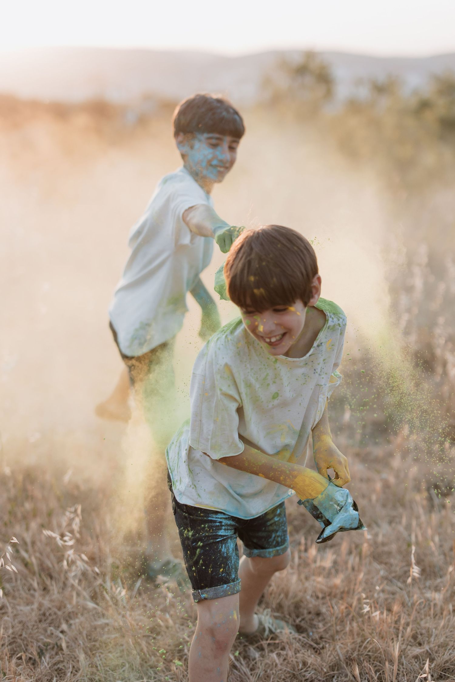 Two children in white shirts play and run through a misty golden field at sunset.