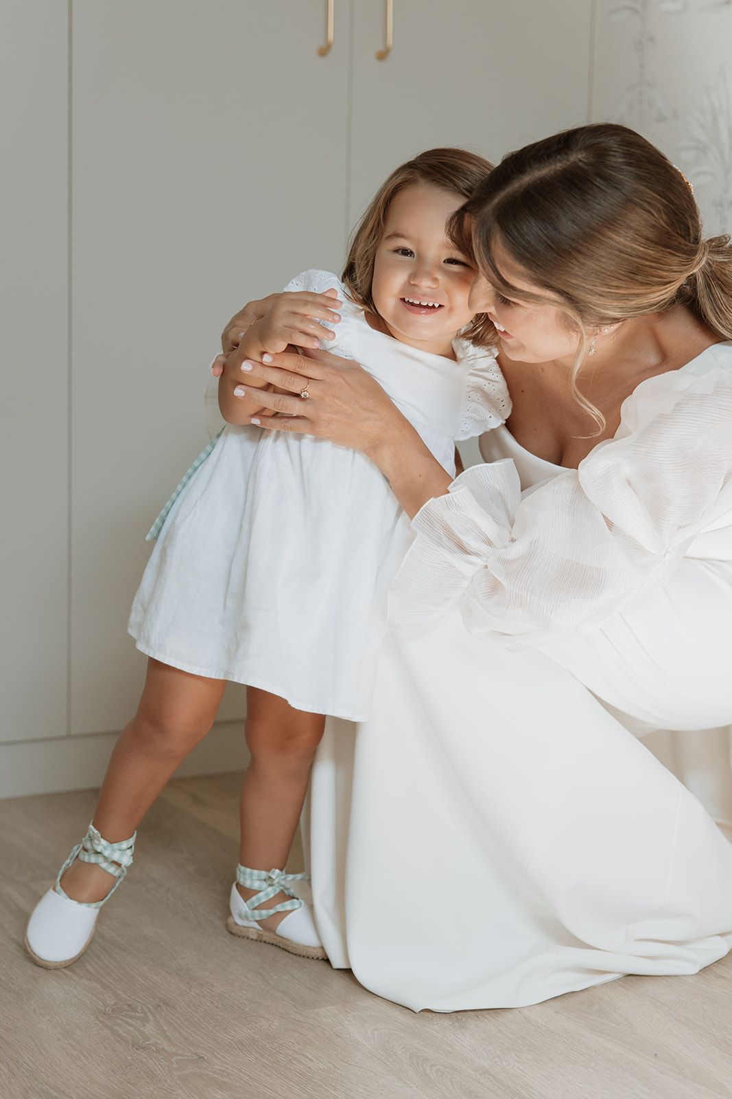 Tender moment shared between two in white dresses against a light interior setting.