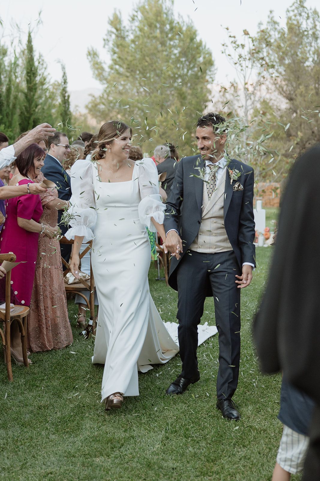 Happy couple walks through shower of confetti at outdoor garden ceremony.