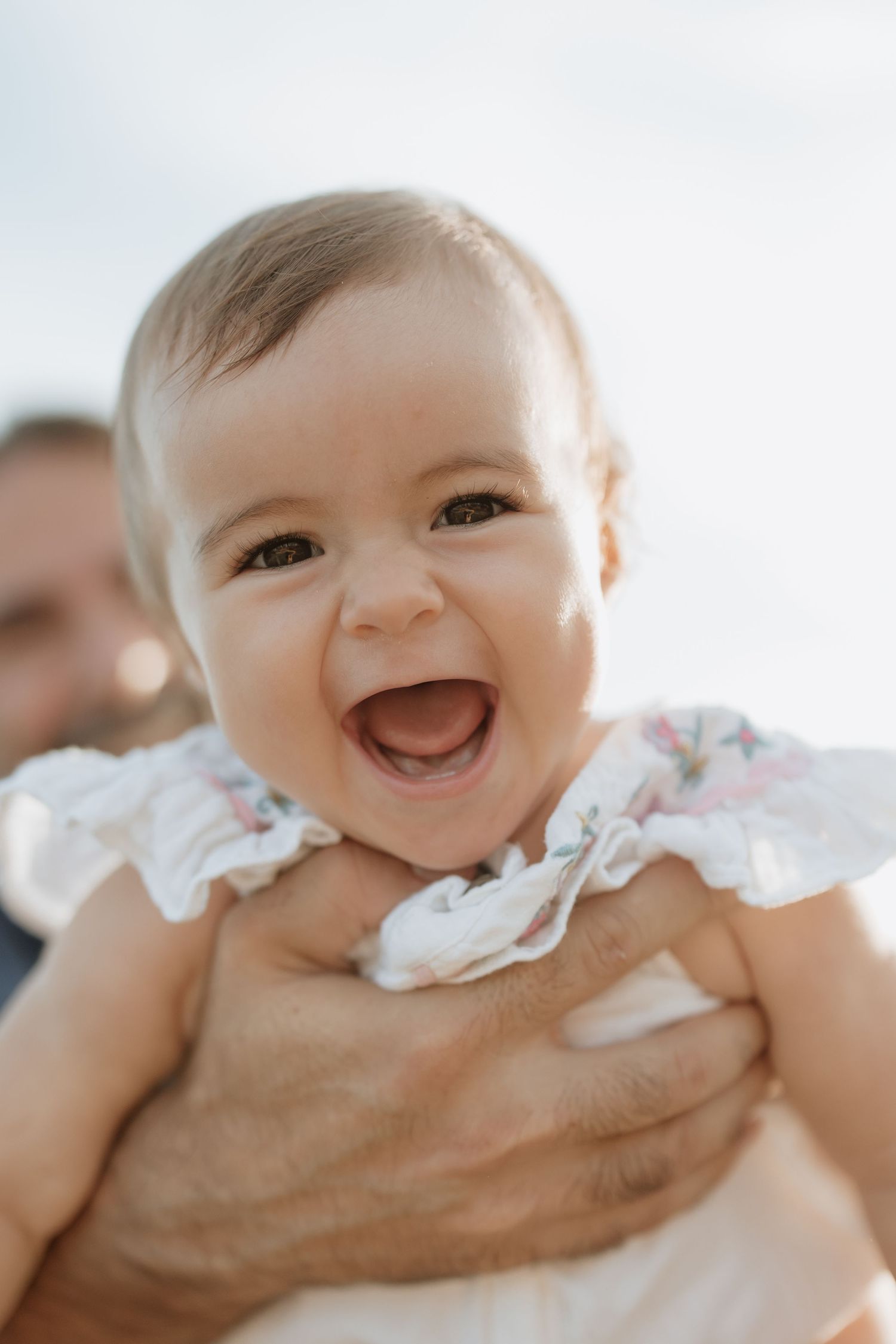 A close-up of a laughing baby with ruffled collar against bright sky.