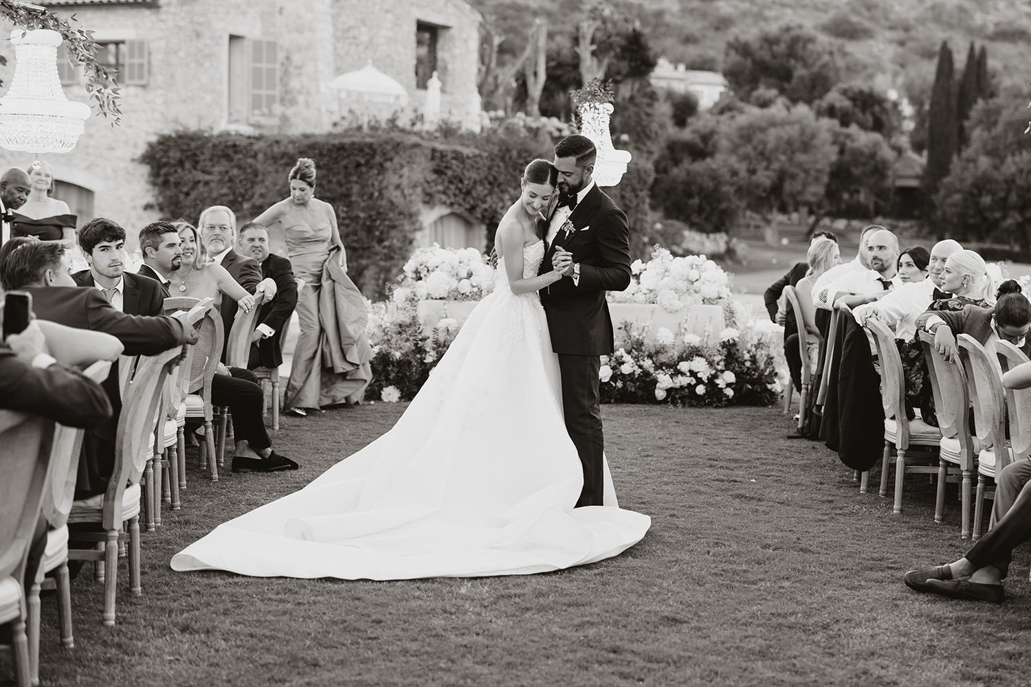 A black and white capture of a wedding ceremony with guests seated on both sides of an outdoor aisle.