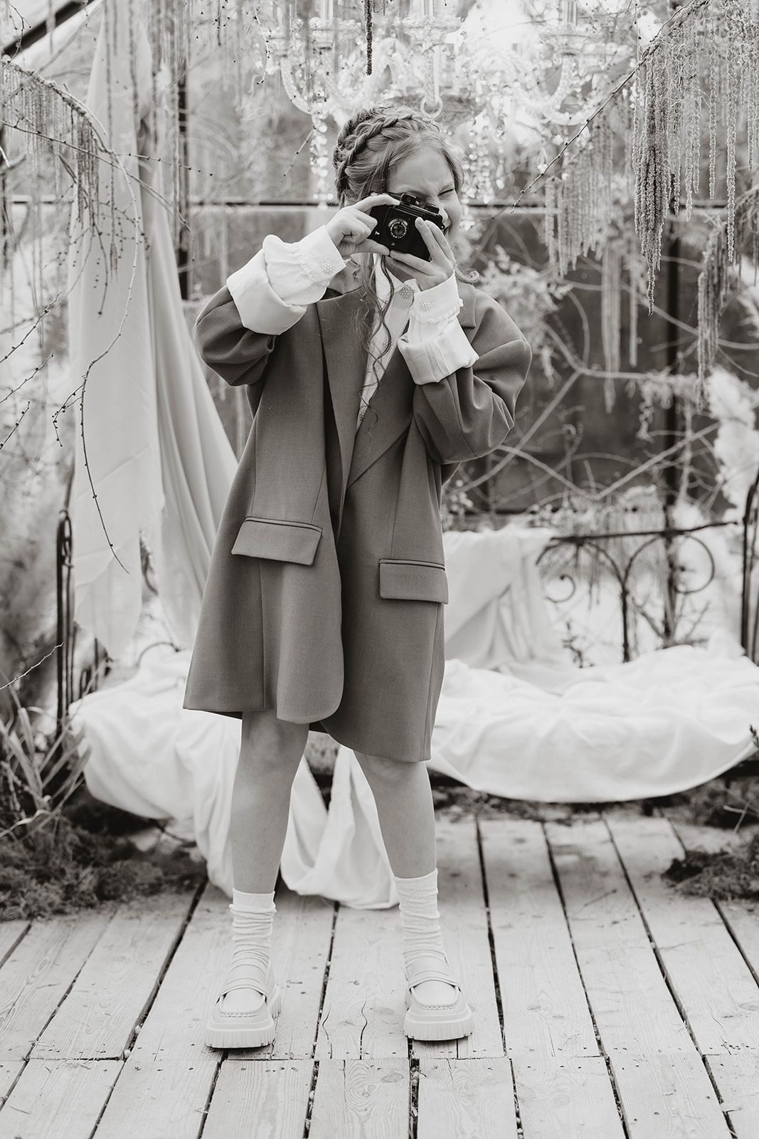 Black and white photo of photographer holding vintage camera on wooden deck with draped fabric.