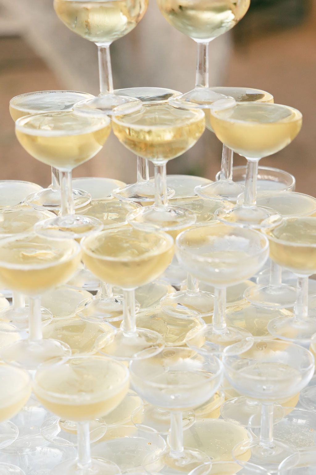Multi-tiered champagne tower with coupe glasses filled with golden bubbly.