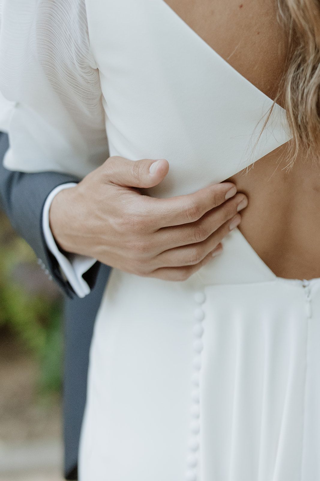 Close-up detail of groom's hand on bride's back showing elegant white wedding dress details.