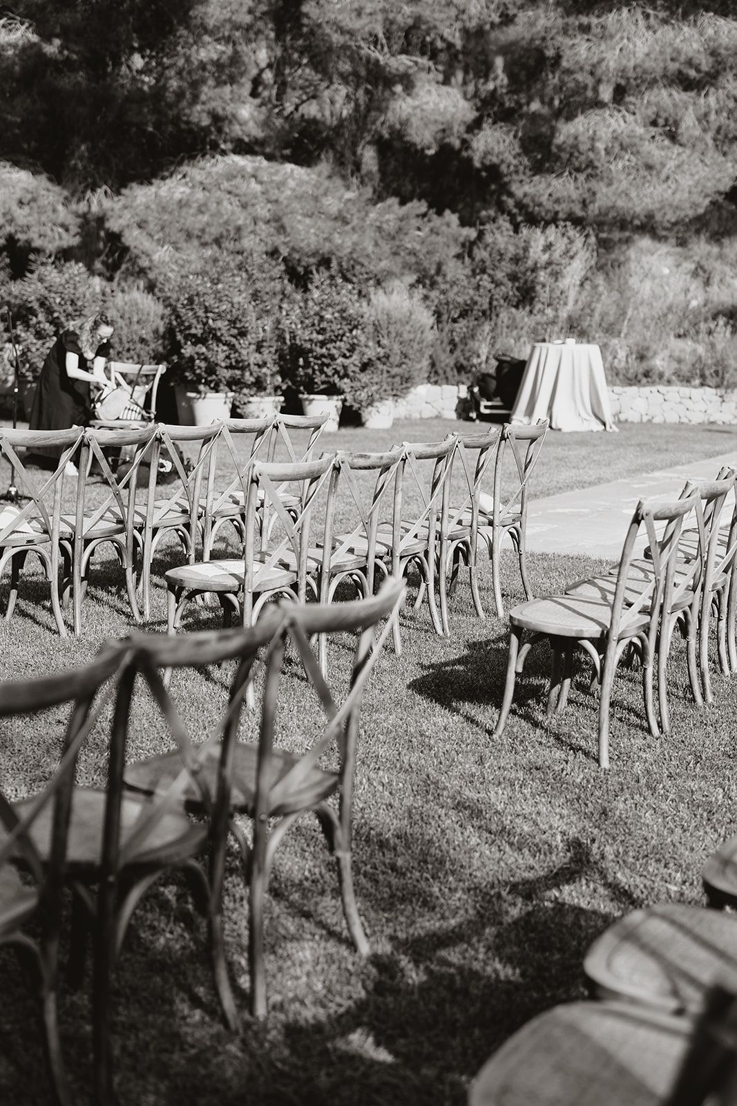 Cross-back chairs set up for an outdoor wedding ceremony with white linens.