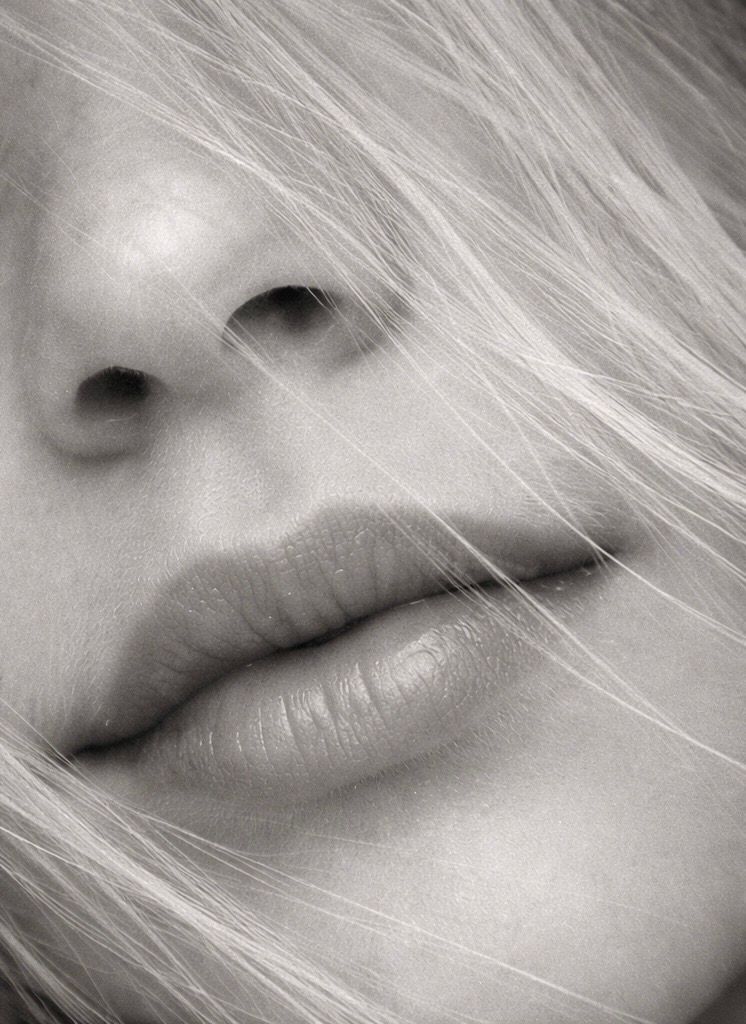 Close-up black and white artistic macro photograph showing nose and lips with wispy blonde hair strands.