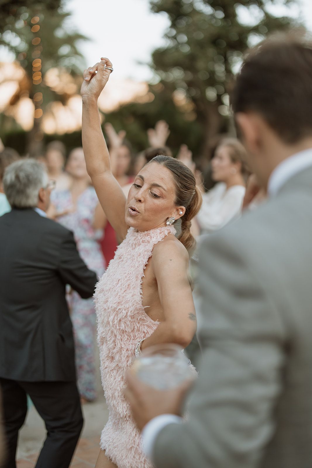Wedding guest in a pink lace dress dances joyfully at an outdoor reception.