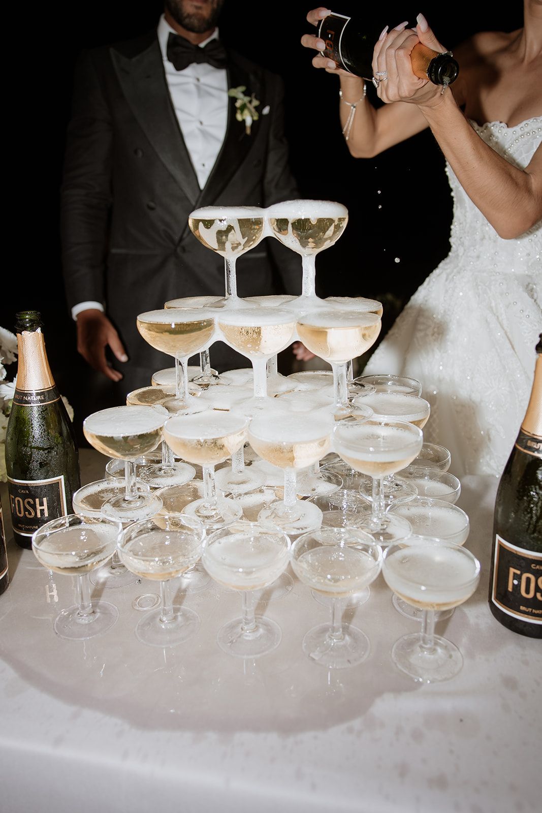 Champagne being poured into a tiered tower of coupe glasses at a formal event.