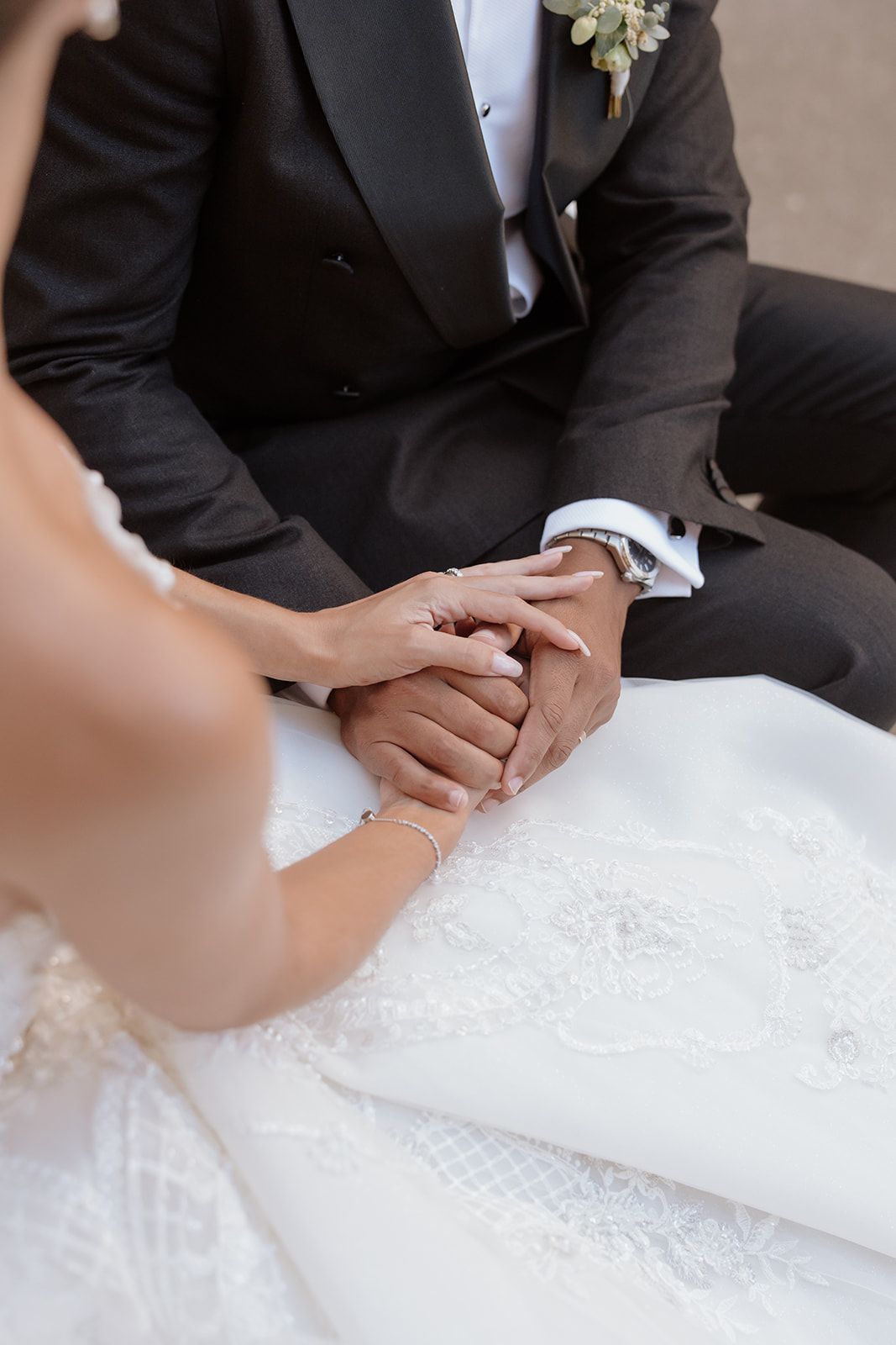 Close-up of clasped hands between couple in wedding attire.
