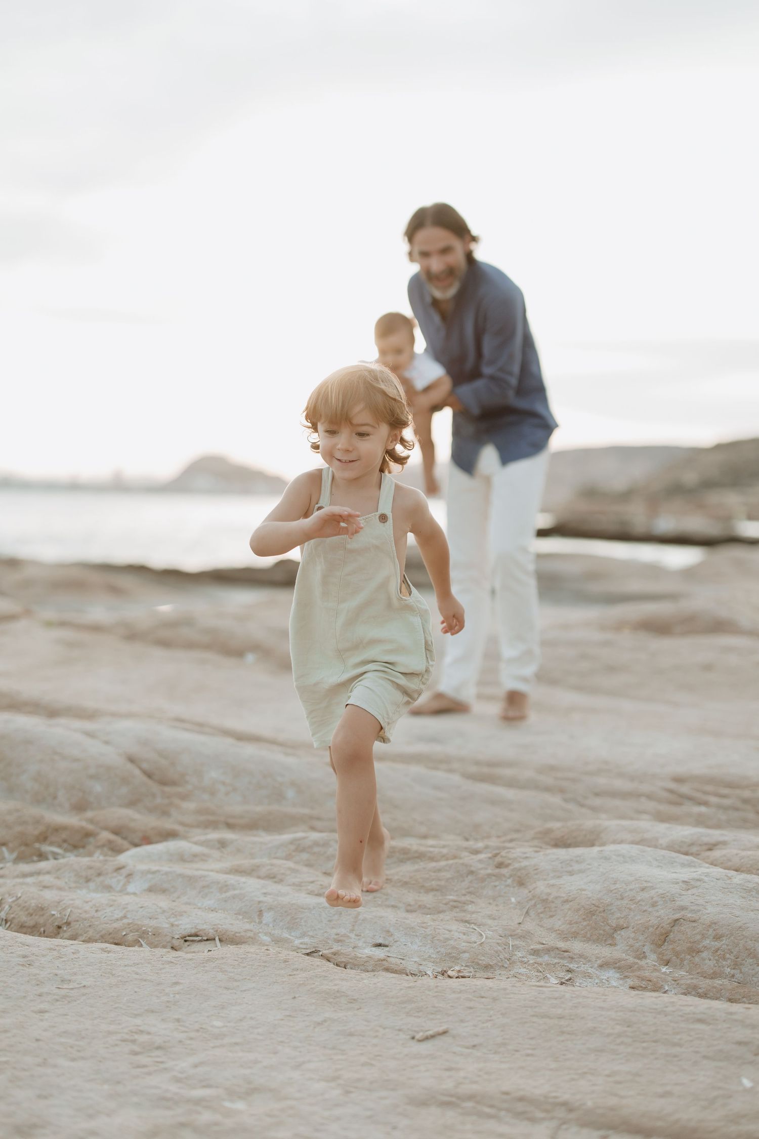 Child running playfully on rocky shore while others watch.
