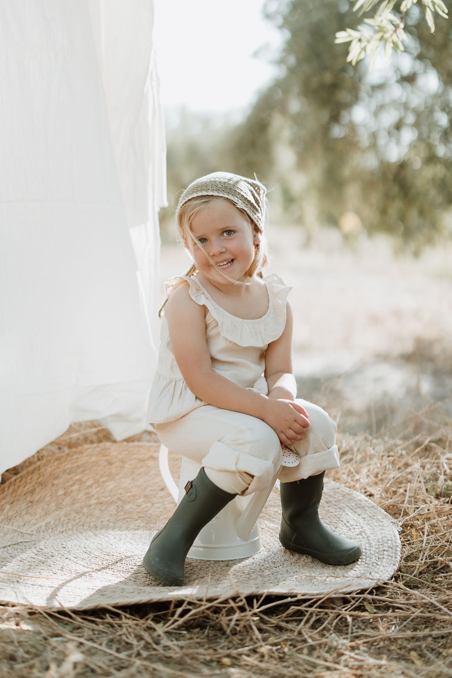 A rustic outdoor photoshoot featuring white linens, a woven mat, and dark boots against a natural setting.
