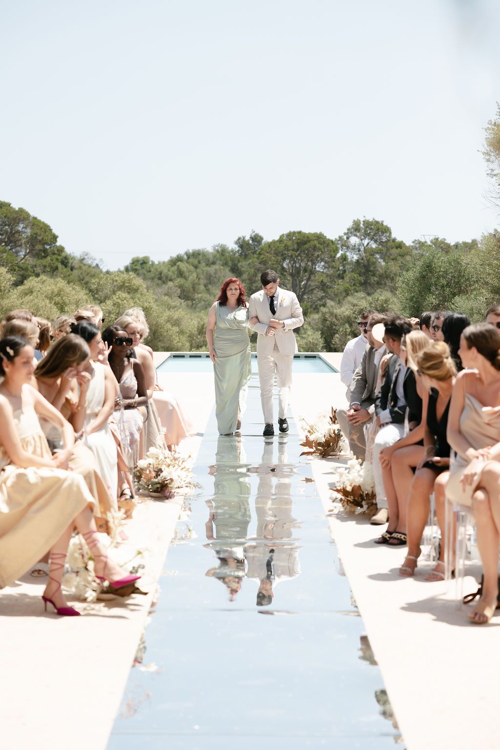 Wedding ceremony on reflective runway with guests seated on both sides in neutral attire.