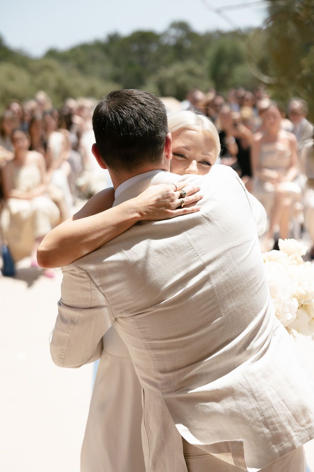 Close-up of an emotional wedding hug between two people wearing white formal attire.