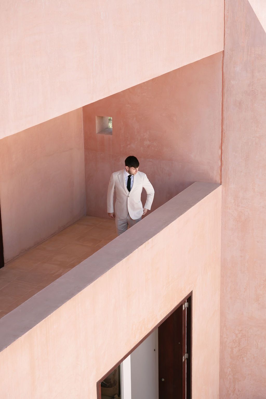 Figure in white suit standing in pink architectural space with geometric lines.