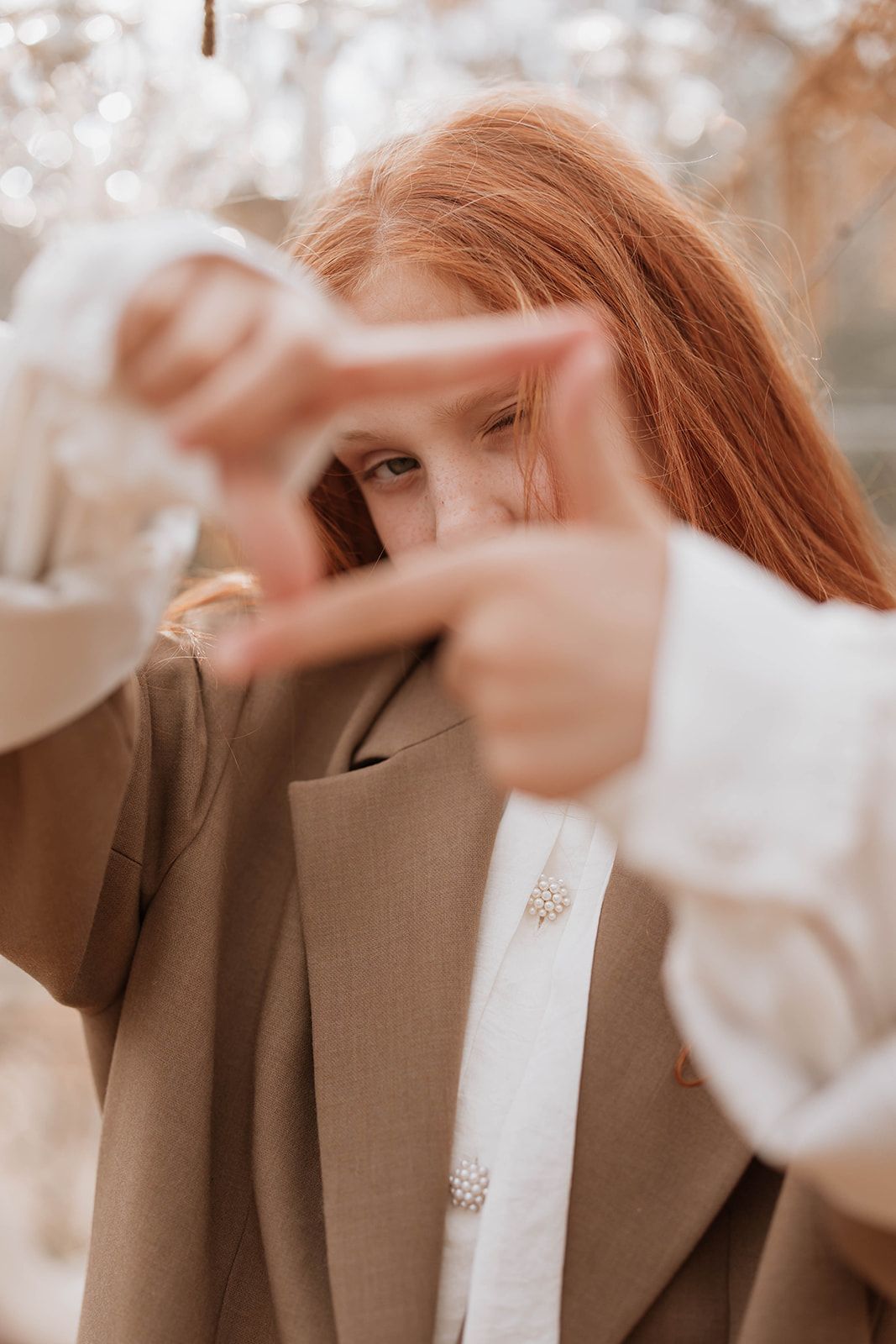 Creative portrait with hands framing the face, wearing a brown coat and white shirt.