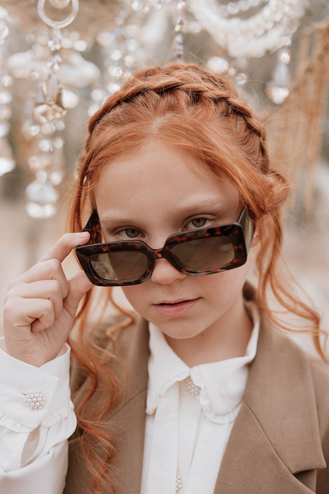 Stylish fashion portrait showing sunglasses and a brown coat against a backdrop of hanging crystals.