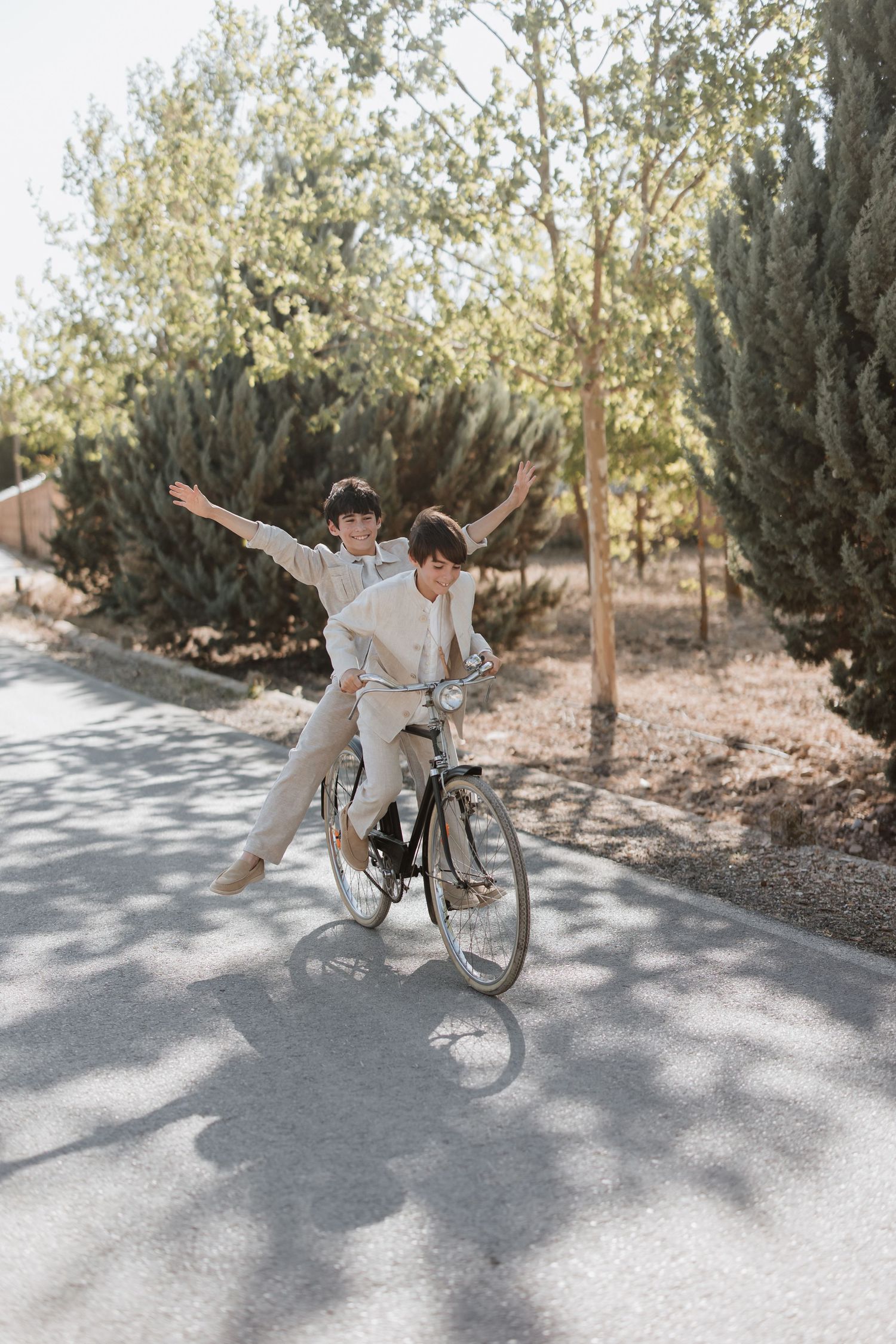 A couple enjoys a playful moment while riding bicycles along a tree-lined path on a sunny day.