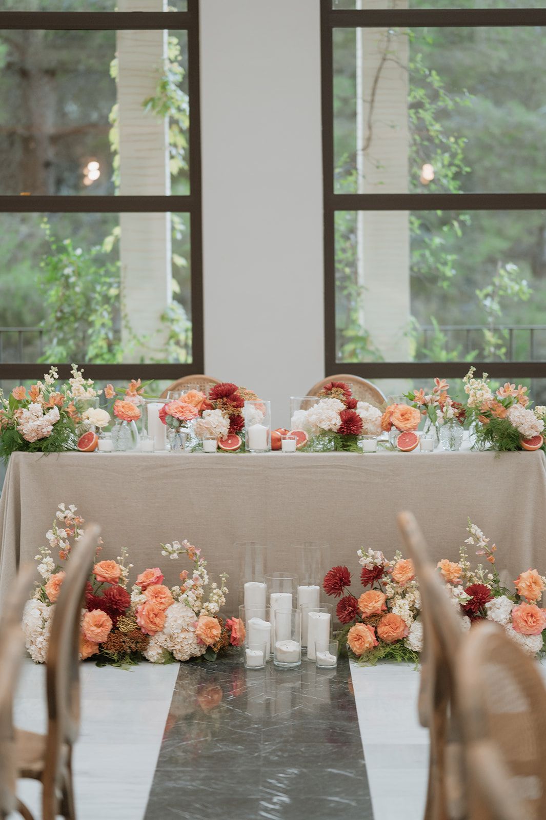 Long reception tables decorated with coral and peach floral arrangements against a window backdrop.