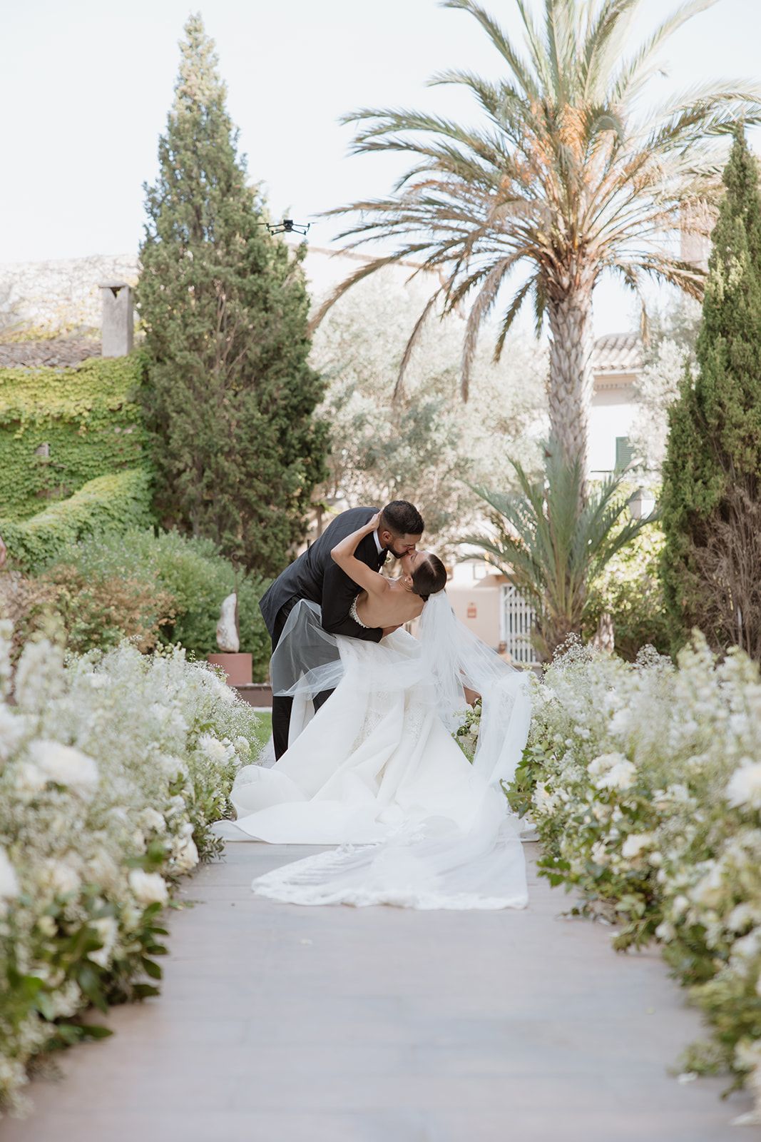 Elegant wedding photos showing a couple in a beautiful garden setting with white flowers and palm trees.