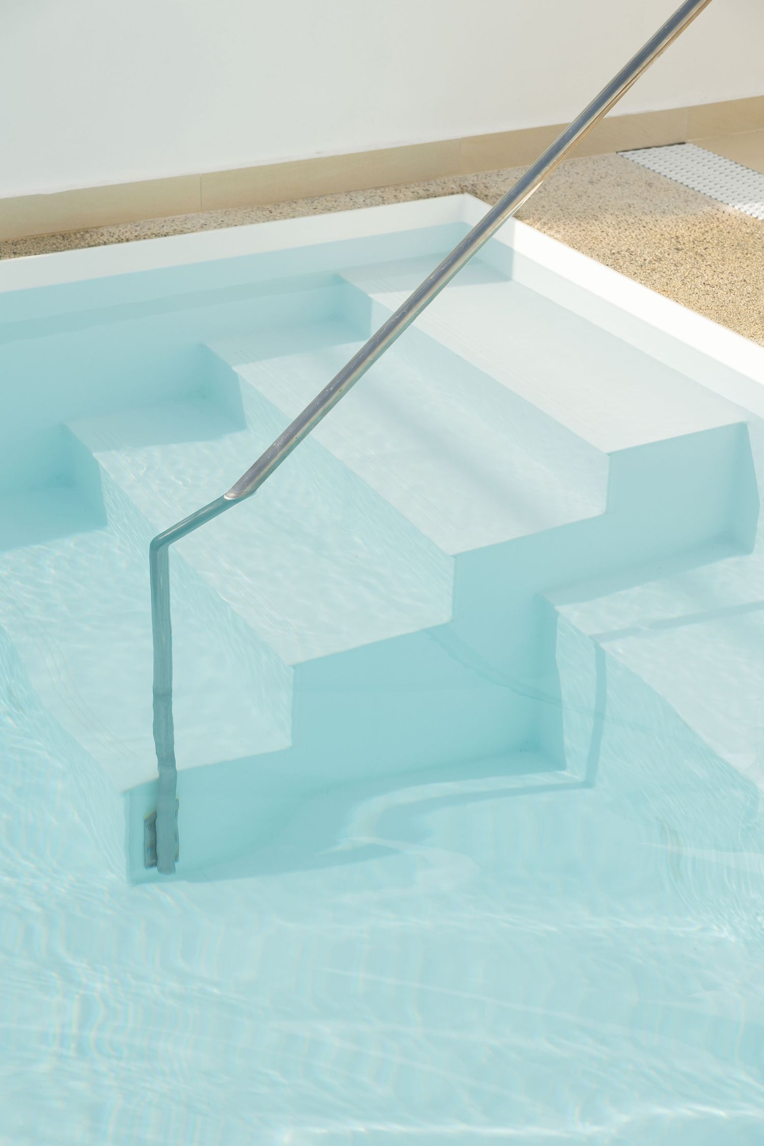 Underwater steps with metal safety rail in a pristine swimming pool with clear turquoise water.