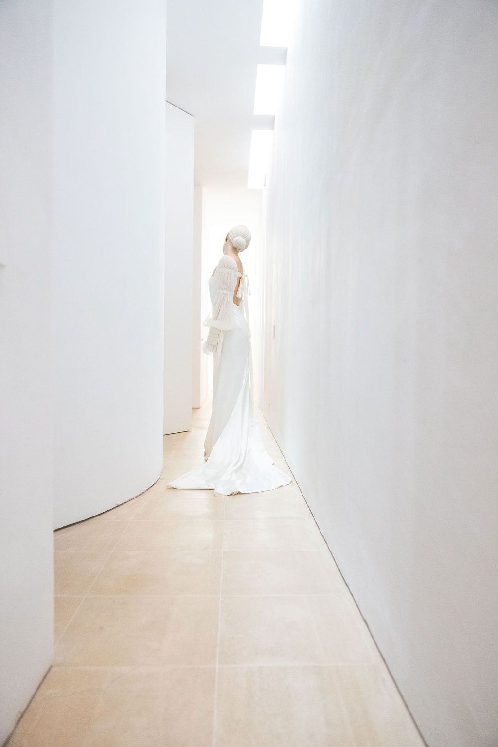 A full-length view of a wedding dress silhouette against white walls in a modern corridor.