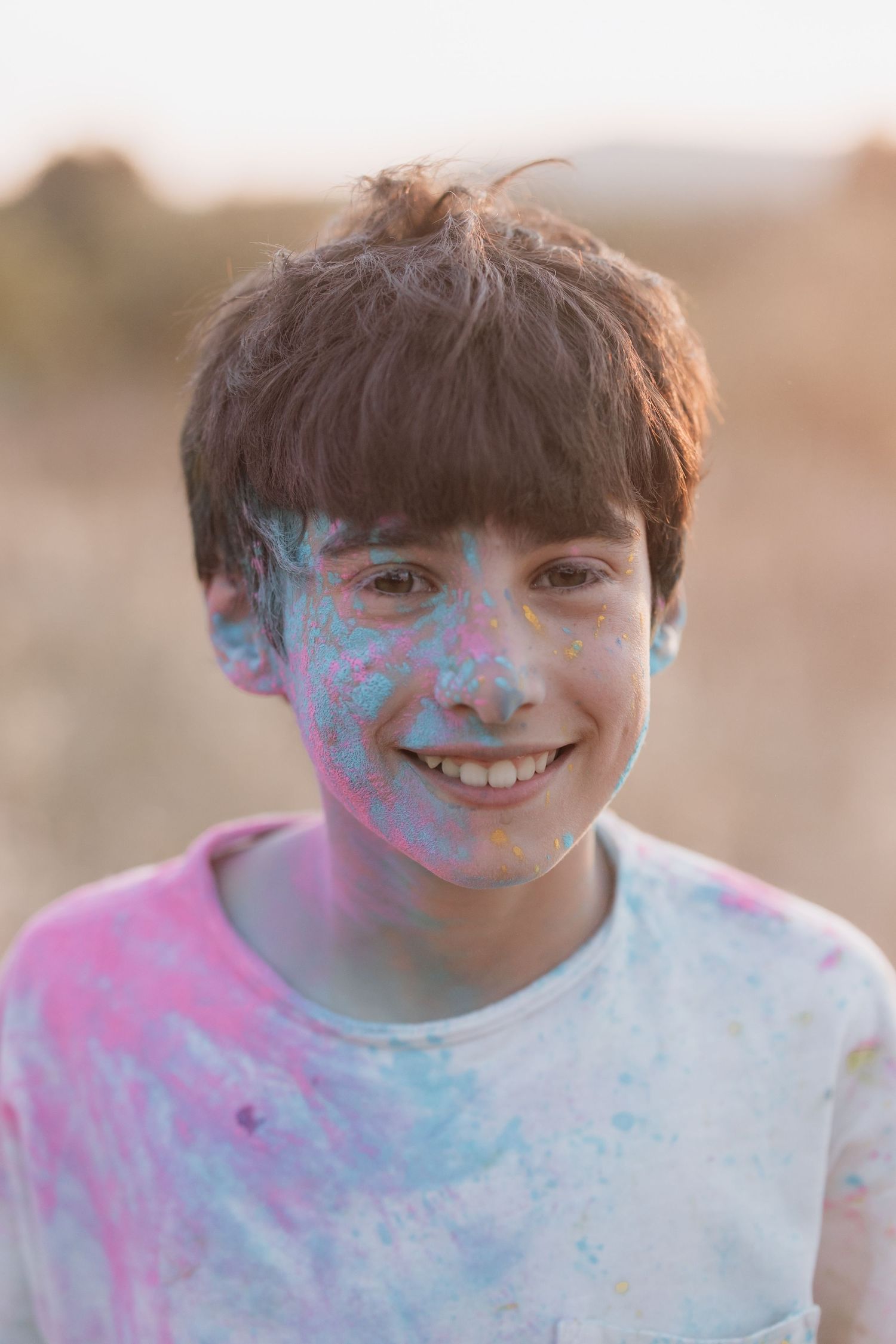 A child covered in blue and pink powder smiles at the camera during what appears to be a color festival or powder event.