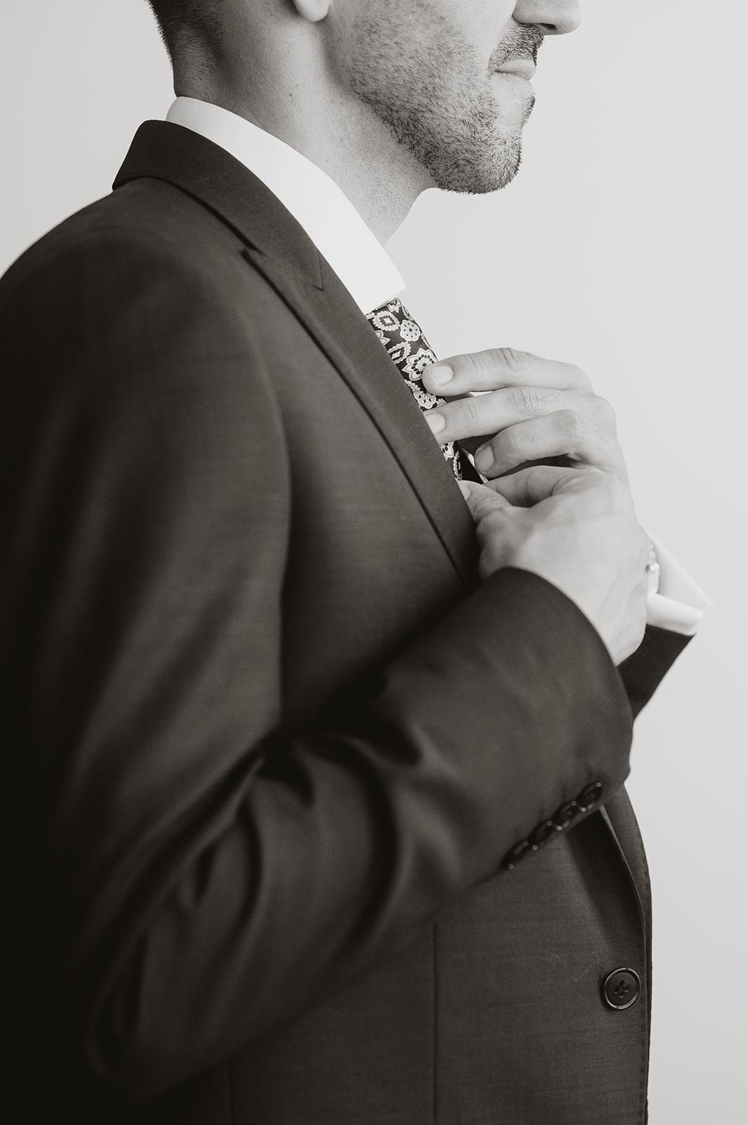 Black and white close-up of someone adjusting their tie while wearing a formal suit.