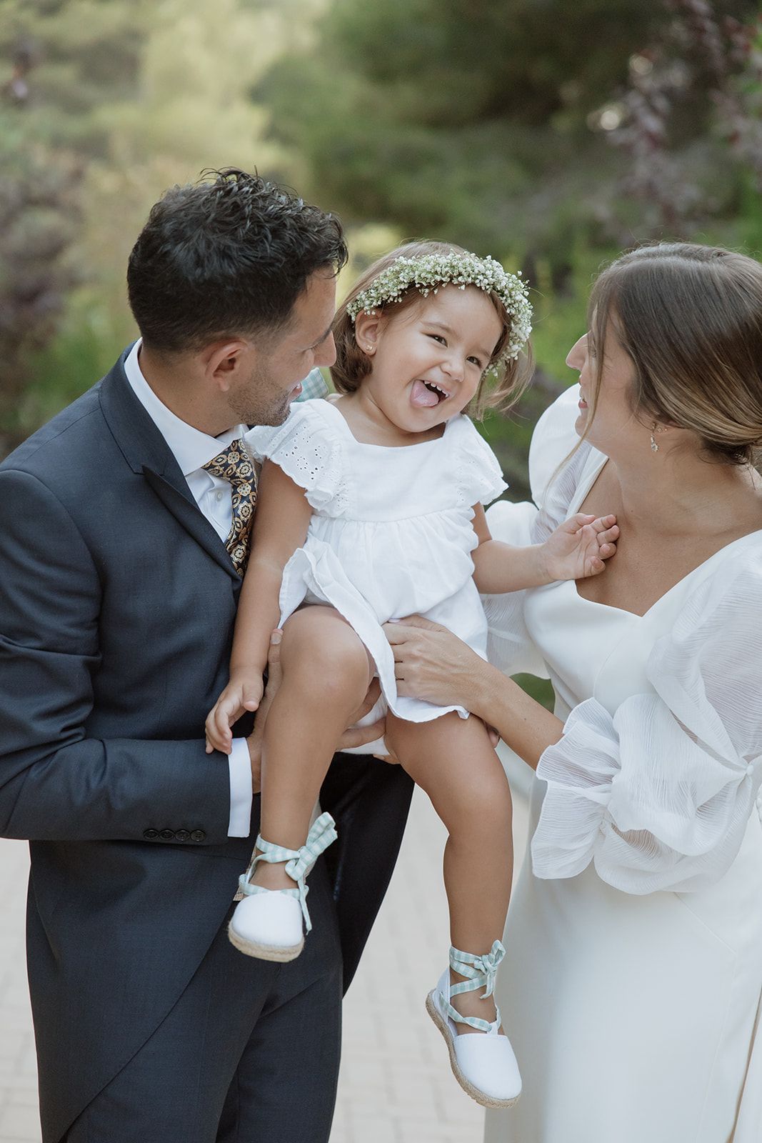 Candid moment of parents laughing with flower girl wearing floral crown.