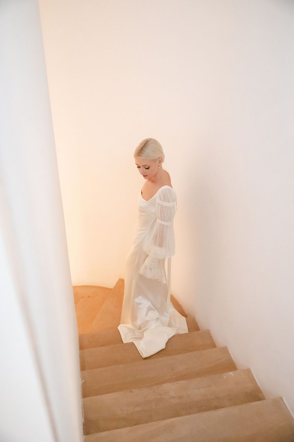 A romantic photograph of a flowing white wedding gown descending stone stairs in soft lighting.