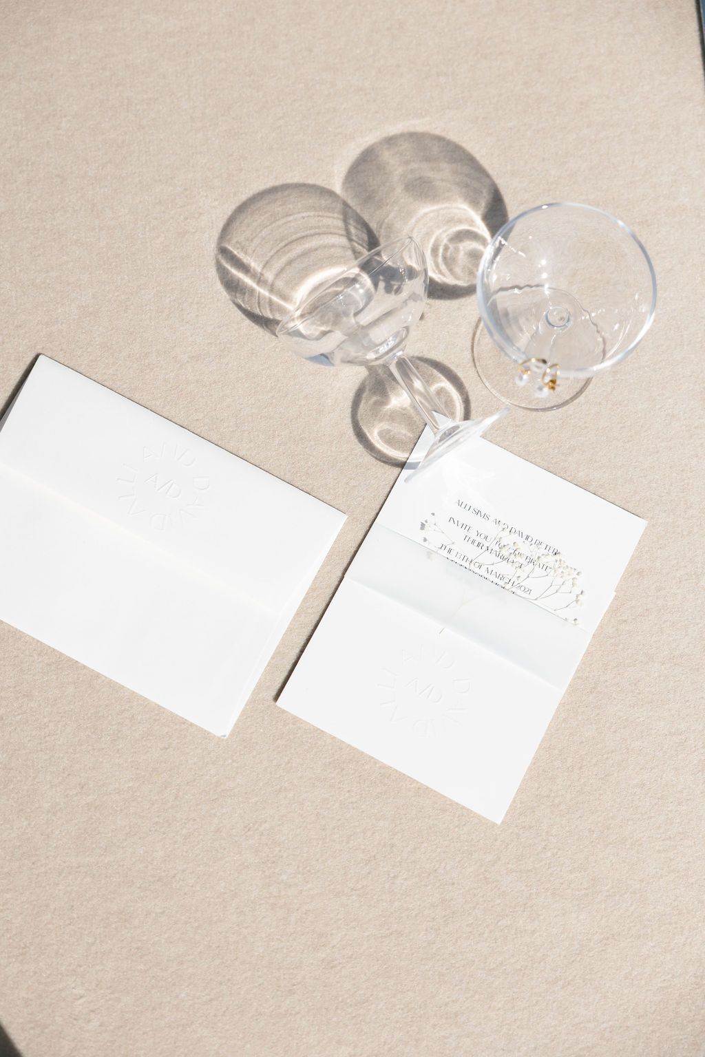 Empty champagne glasses and white stationery arranged on neutral beige background.