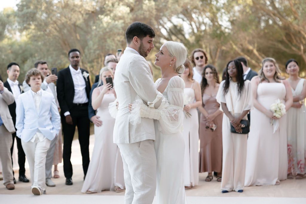 Wedding couple shares an intimate moment surrounded by guests wearing soft neutral colors.