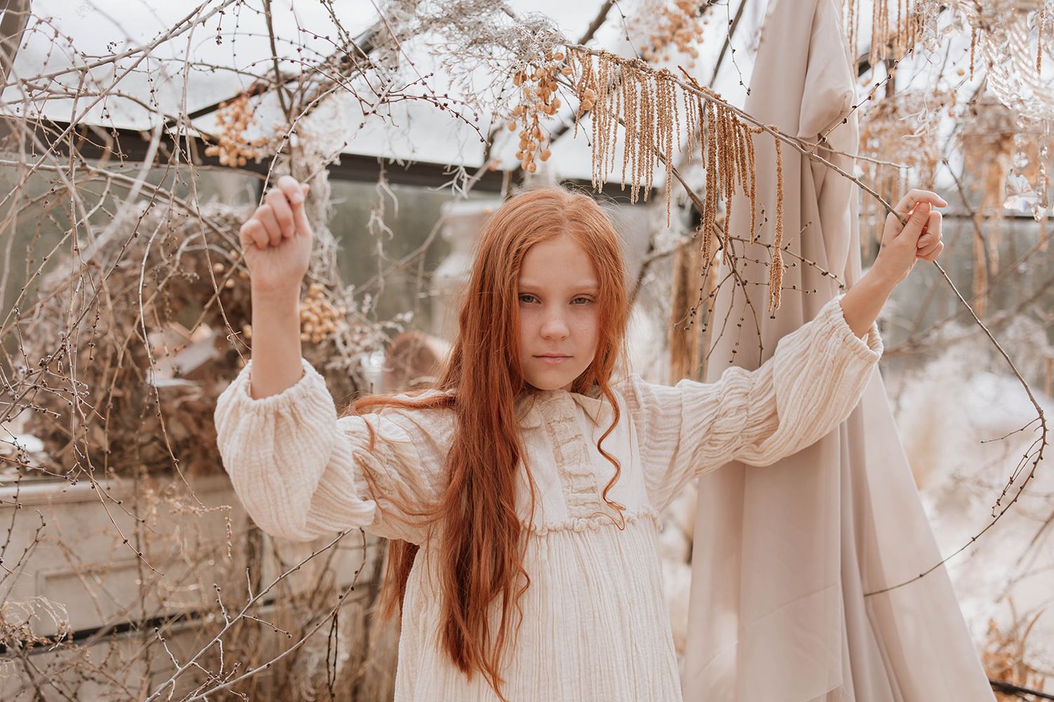 Rustic outdoor portrait with flowing white dress among winter branches.