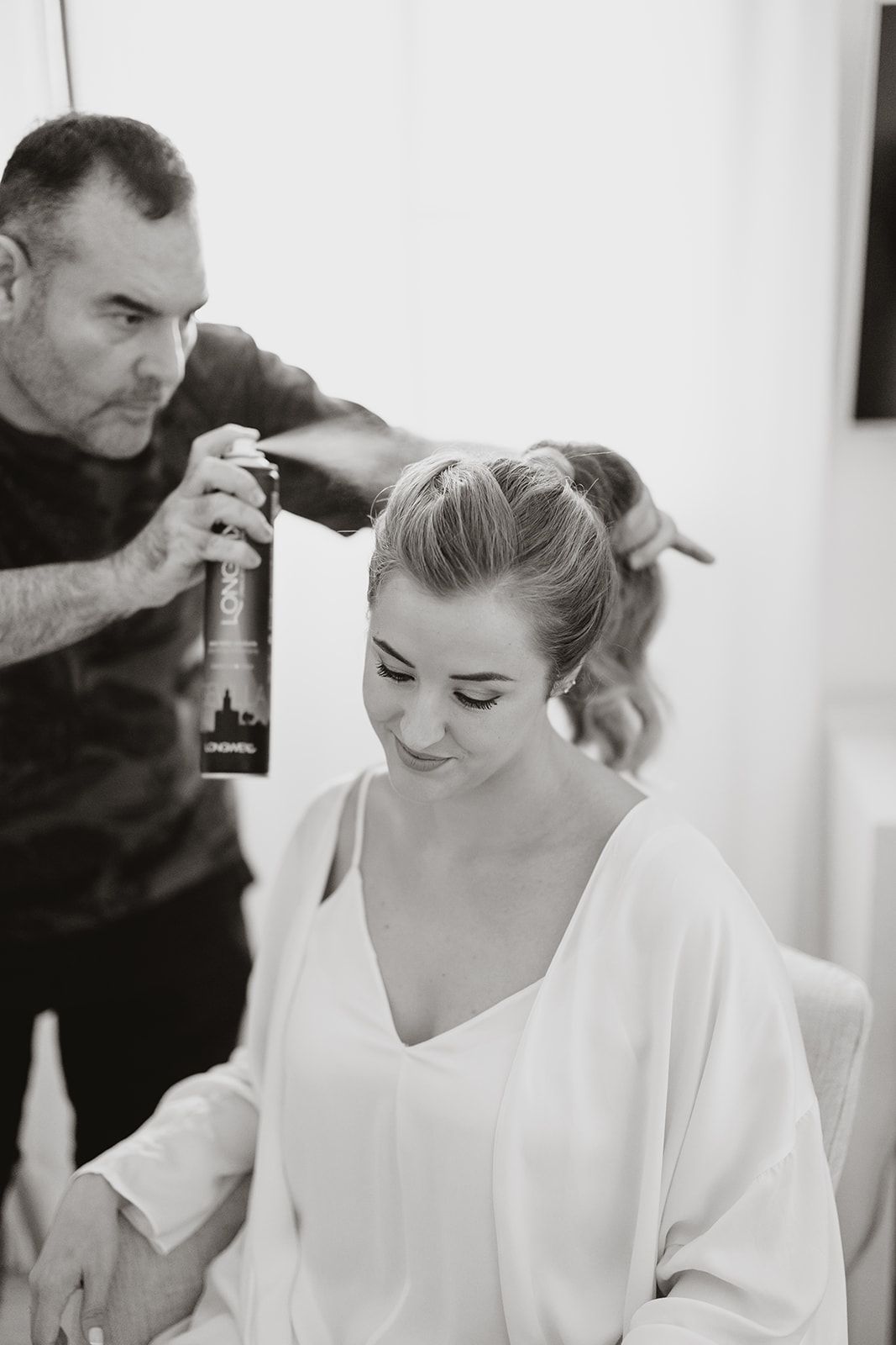 Hair stylist applying product while styling bride's updo during wedding preparation.