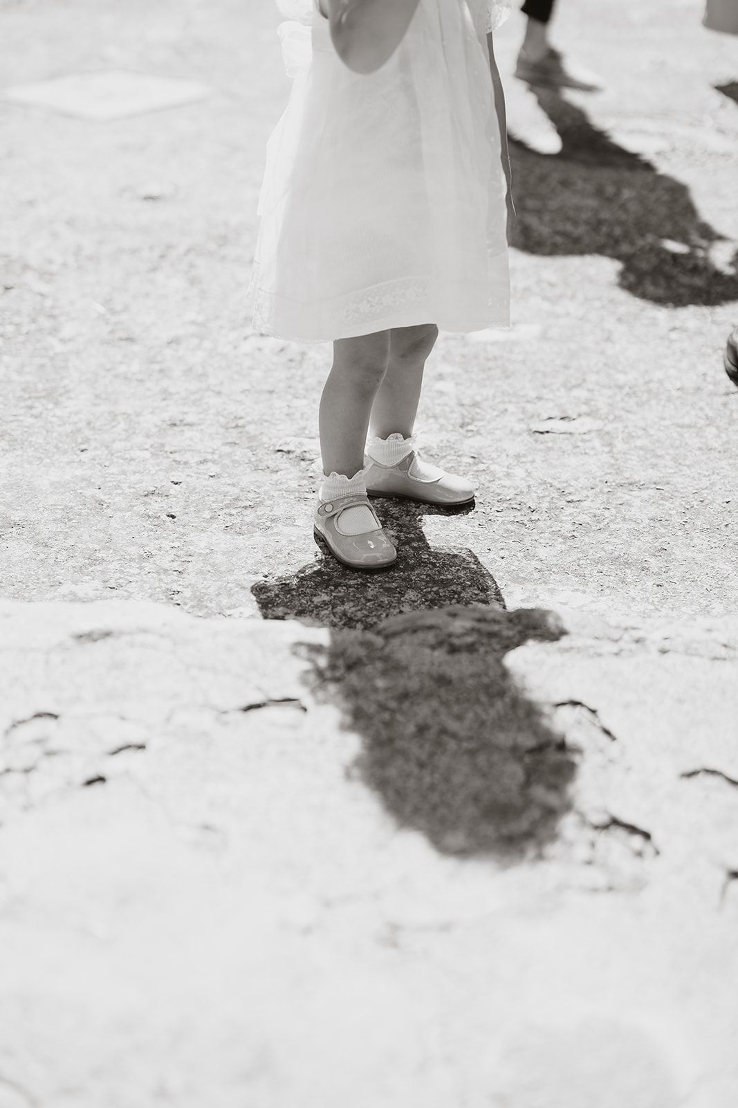 Black and white detail of small feet in dress shoes casting shadow on stone ground.