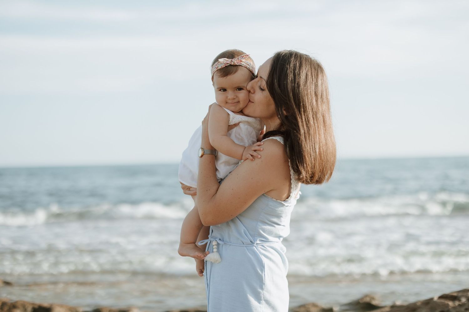 A tender beach photoshoot showing embraces against an ocean backdrop with soft natural lighting.
