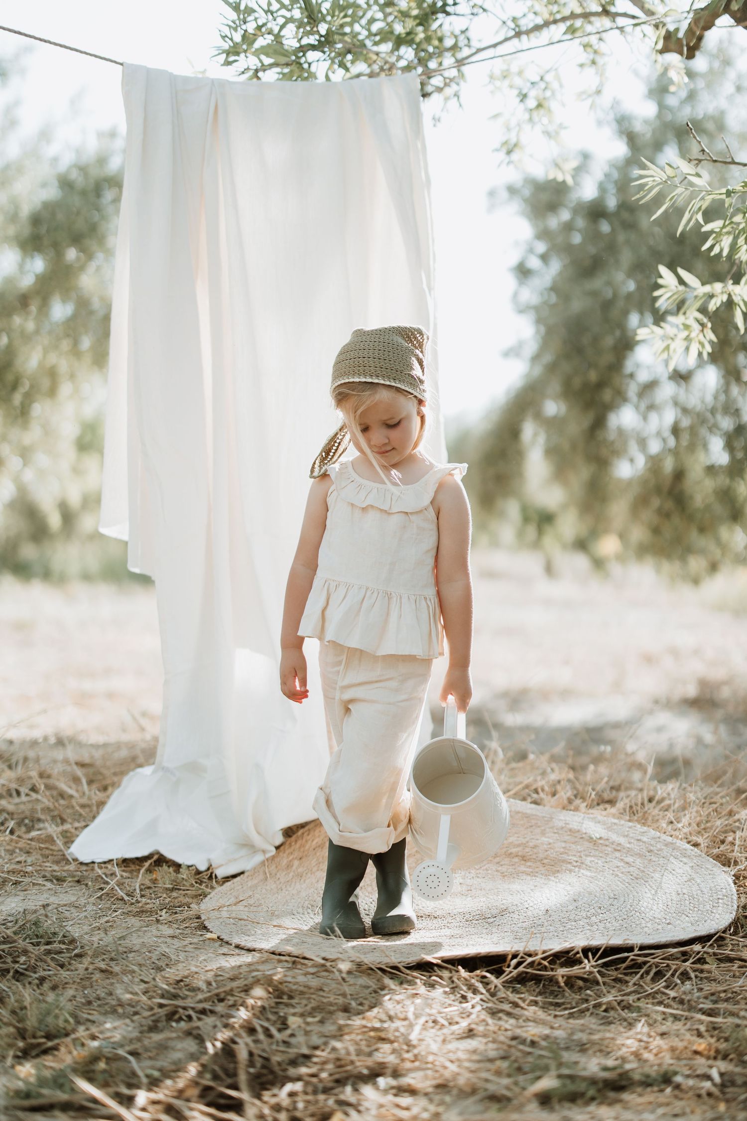 Outdoor scene with white hanging linens and woven mat showcasing vintage-style clothing and boots.