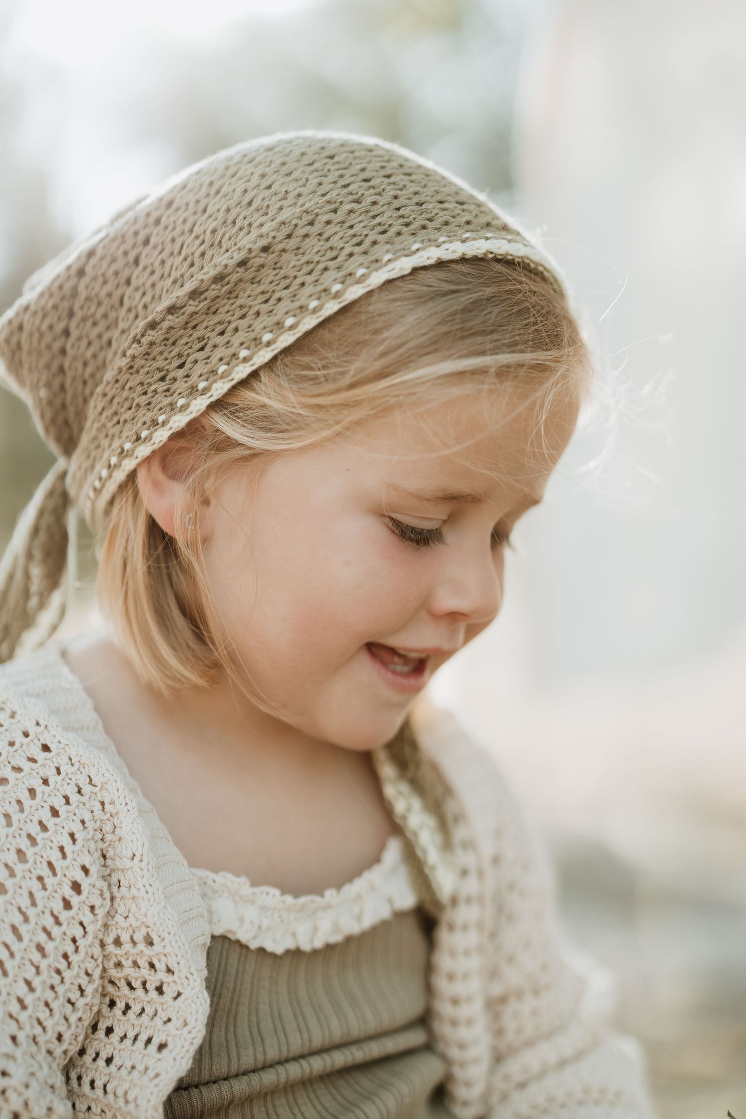 A young figure wearing a knit headband and sweater looks down with a gentle smile.