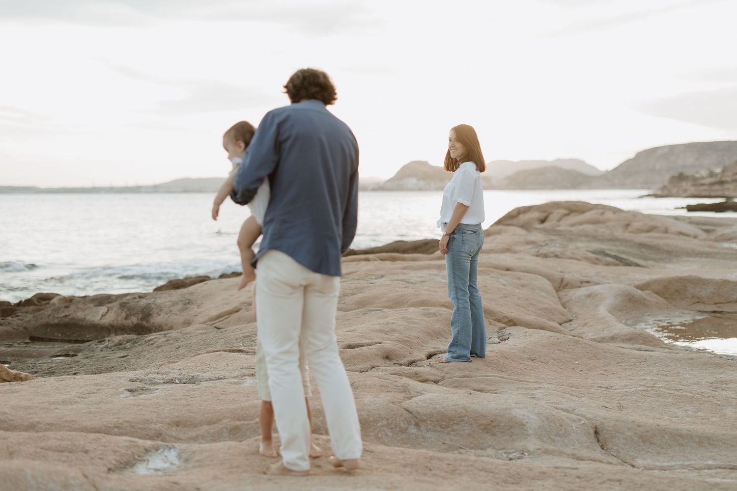 Family explores rocky coastline together during sunset by the ocean.