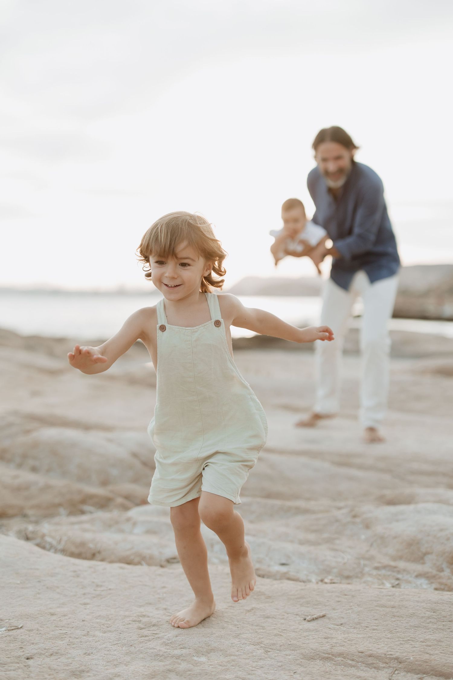 Child running joyfully on a beach at sunset while others follow behind.