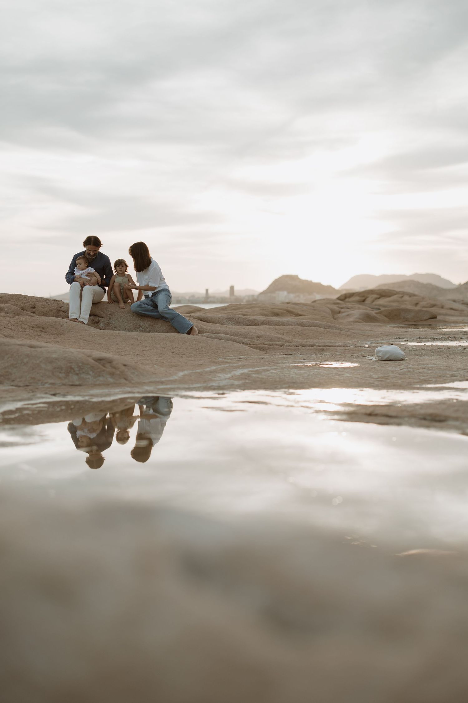 Peaceful gathering on coastal rocks with reflection in calm water below.