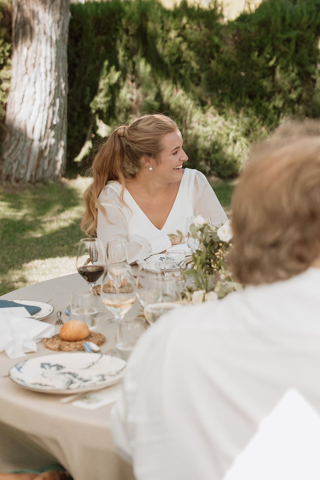 Bride smiling during outdoor wedding reception seated at decorated table.