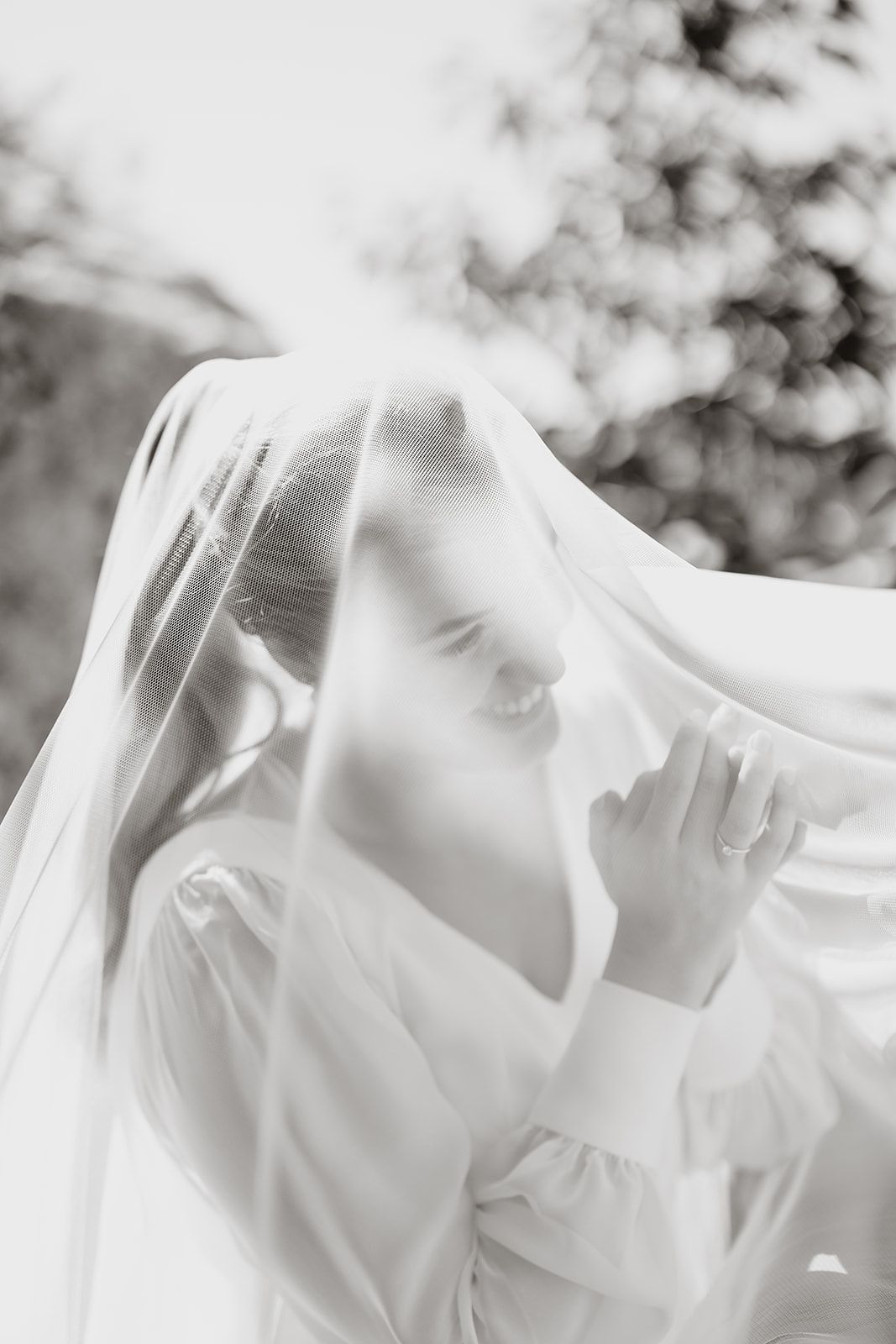Artistic black and white photo of bride beneath flowing veil creating dreamy atmosphere.