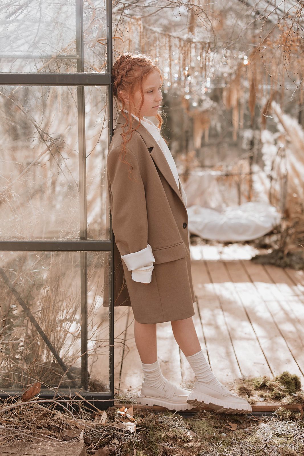 Side view of someone in a brown blazer standing inside a greenhouse with winter scenery.