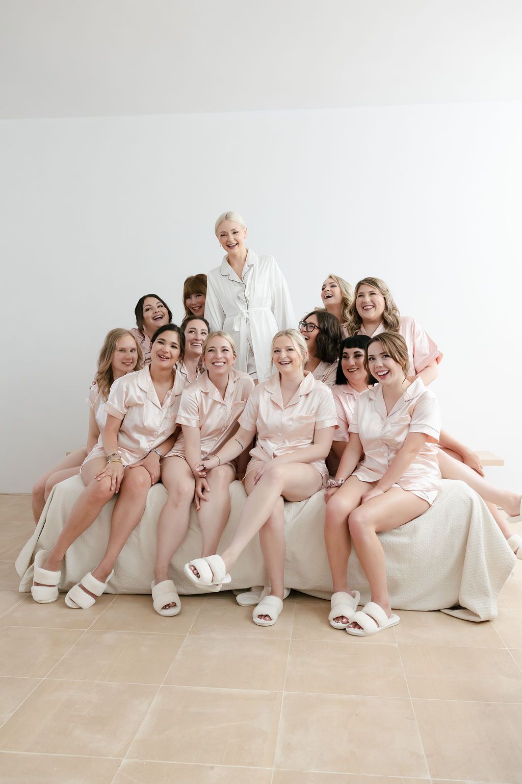 Group wearing matching pink satin pajamas and white slippers pose together on light background.